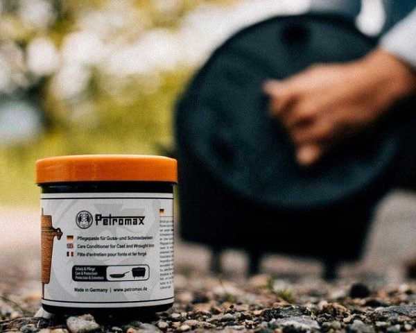 Pasta de intretinere Petromax pentru fonta si fier cu persoana care ridica capacul unui ceaun pe fundal